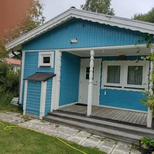 Blå trästuga med veranda, vita knutar och trappa