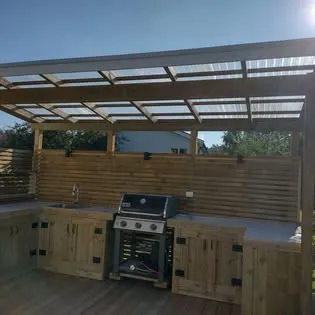 Utekök i trä med grill under en pergola med genomskinligt tak
