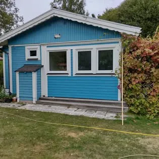 Blå stugfasad med vita fönster, trappa och gräsmatta