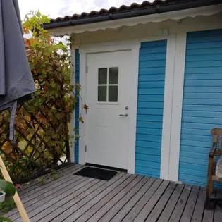 Vit entrédörr i en blå panelfasad, framför ett trädäck
